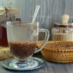 Szklanka z wodą i siemieniem lnianym, obok miód i koszyk z nasionami. Kiedy pić siemię lniane rano czy wieczorem? To pytanie o zdrowie.