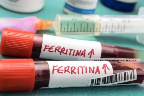 Dwie probówki z krwią oznaczone "Ferritina" i strzałką w górę, sugerujące potrzebę podniesienia ferrytyny. Obok strzykawka i fiolki.