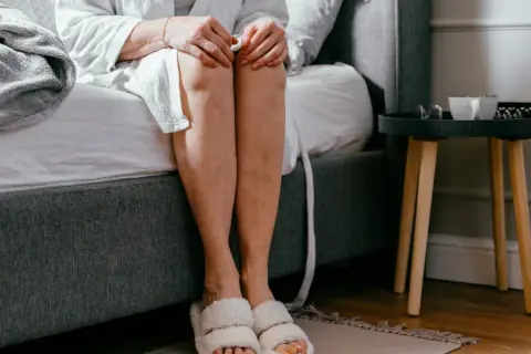 Kobieta w szlafroku i kapciach siedzi na łóżku, rozważając domowe sposoby na nietrzymanie moczu.